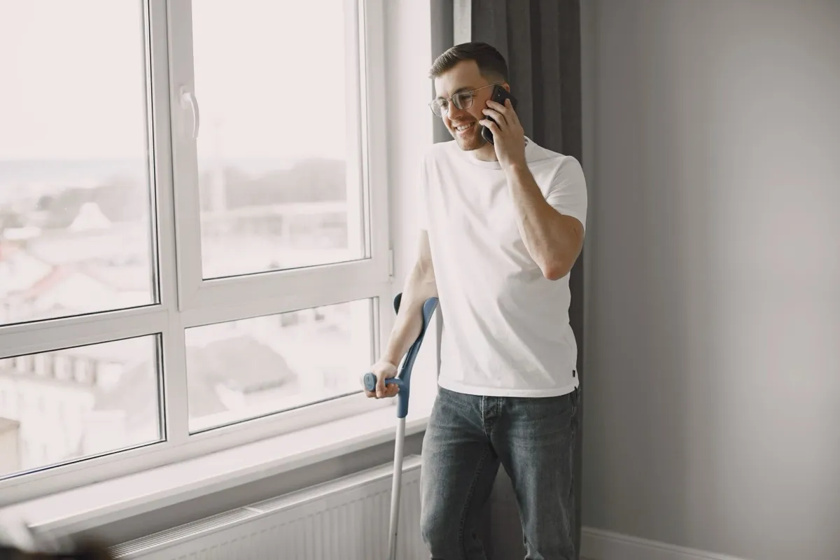Hombre con una muleta hablando por teléfono junto a una ventana