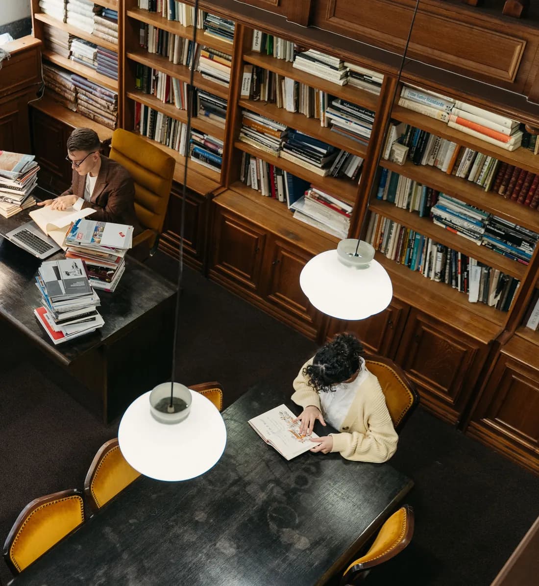 Personas estudiando con libros y apuntes en una biblioteca de estanterías de madera
